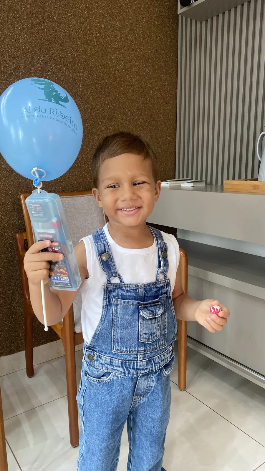 Menino de macacão jeans segurando o balão azul do consultório