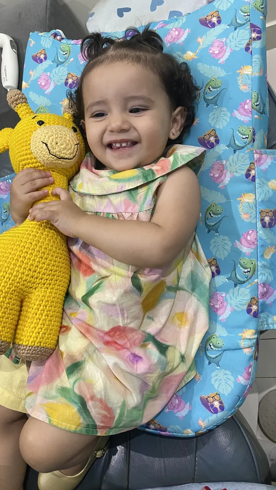 Bebê sorrindo na cadeira, abraçada a uma girafa de crochê
