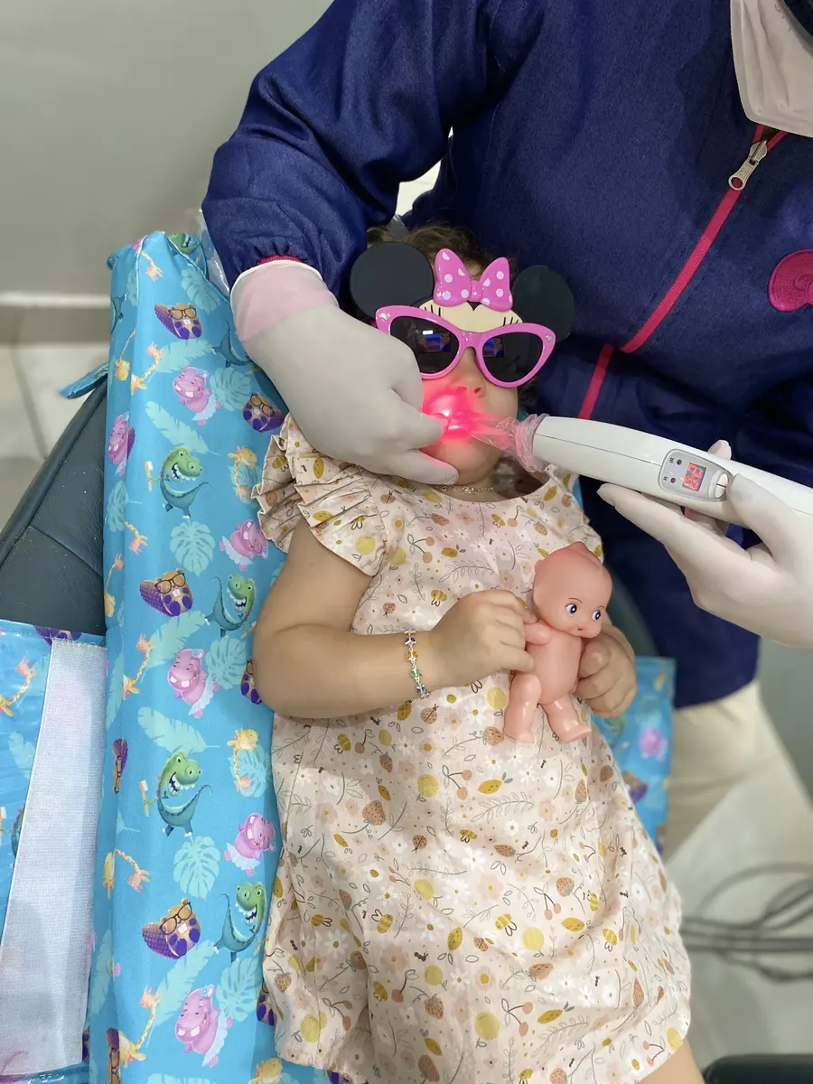 Aplicação de laserterapia em uma bebê que segura uma boneca