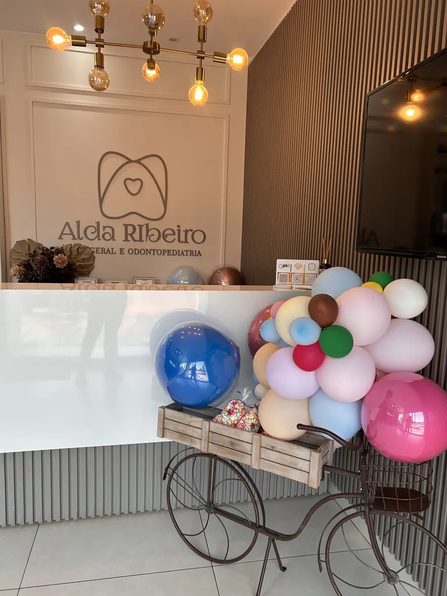 Recepção do consultório com a logo Alda Ribeiro na parede e uma bicicleta cheia de balões
