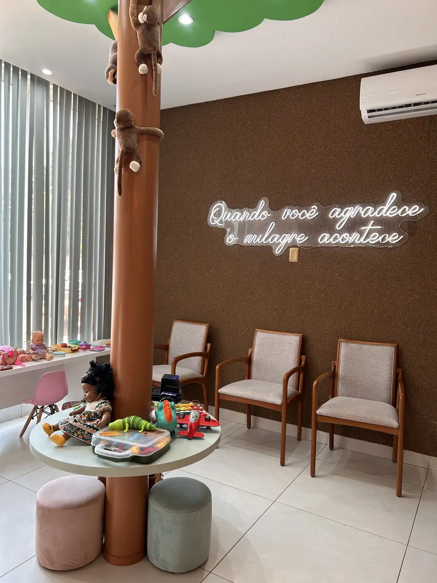 Sala de espera com árvore, mesa de brinquedos e o letreiro Quando você agradece o milagre acontece